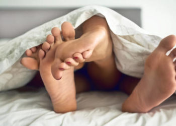 Shot of a couple’s feet poking out from under the bed sheets